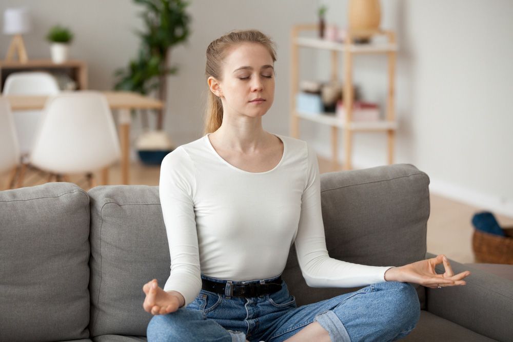 A Woman Is Sitting On A Couch In A Lotus Position With Her Eyes Closed — Wegner Therapies In Pialba, QLD
