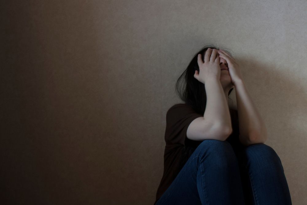 A Woman Is Sitting On The Floor Covering Her Face With Her Hands — Wegner Therapies In Pialba, QLD
