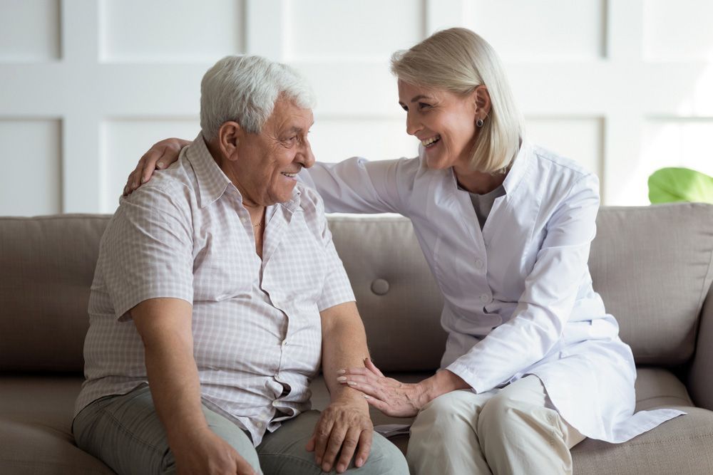 A Nurse Is Sitting On A Couch With An Elderly Man — Wegner Therapies In Pialba, QLD