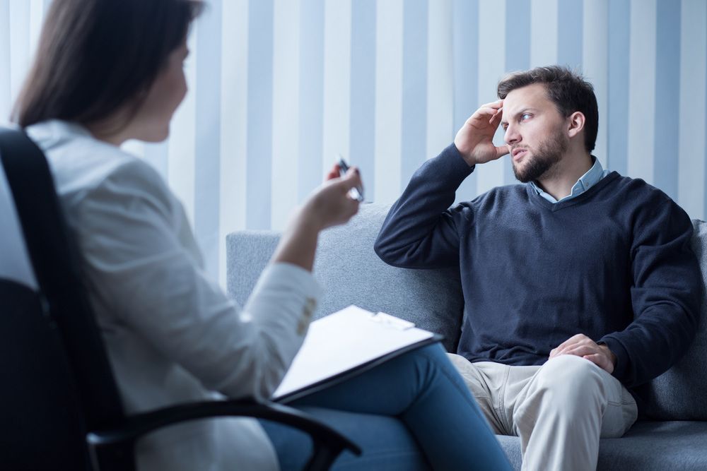 A Man Is Sitting On A Couch Talking To A Woman — Wegner Therapies In Pialba, QLD