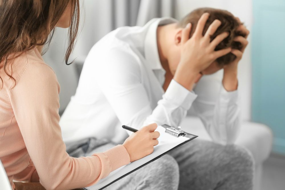 A Woman Is Sitting Next To A Man With His Head In His Hands — Wegner Therapies In Pialba, QLD
