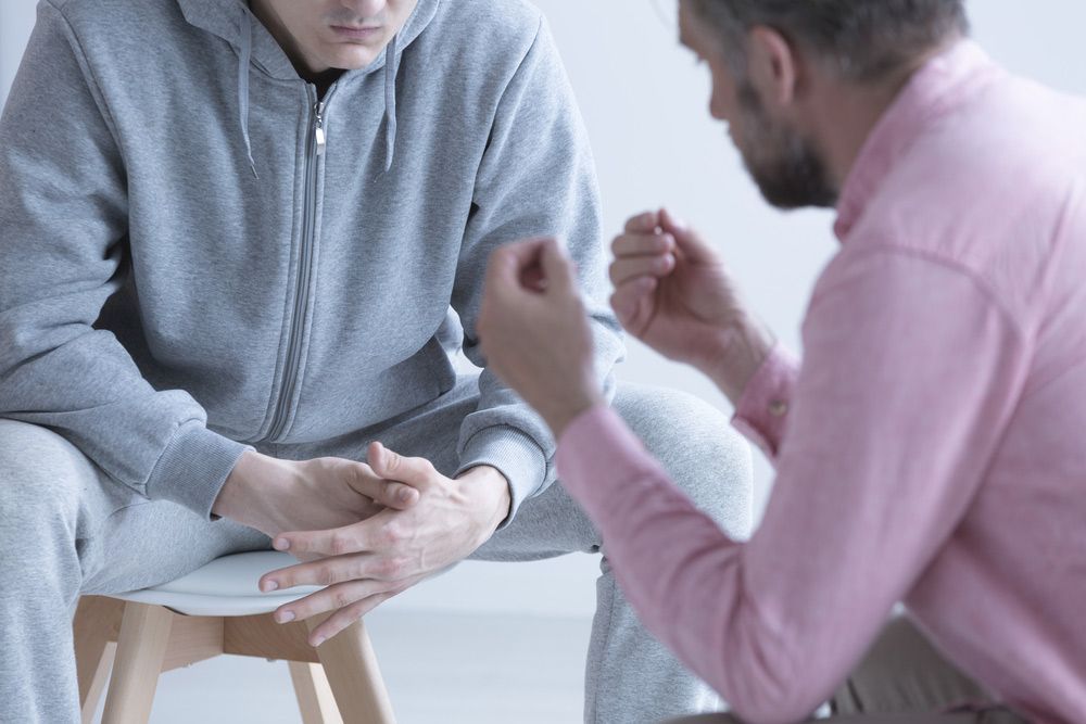 A Man In A Pink Shirt Is Talking To A Man Sitting On A Stool — Wegner Therapies In Pialba, QLD