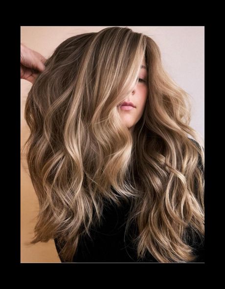 Woman with long, wavy brown hair highlighted with blonde, styled with volume.
