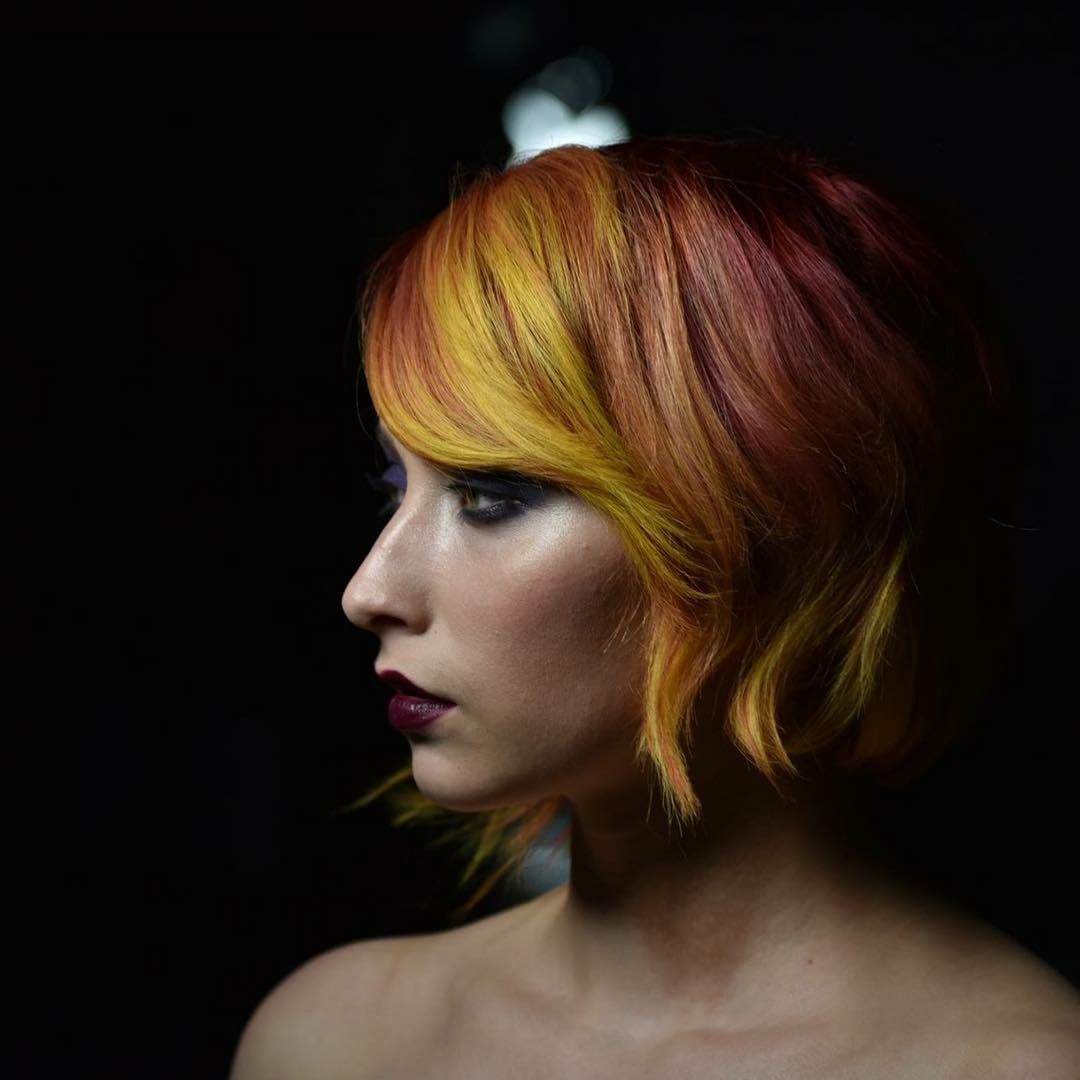 Woman with auburn and yellow hair in profile, dark makeup, looking left. Black background.