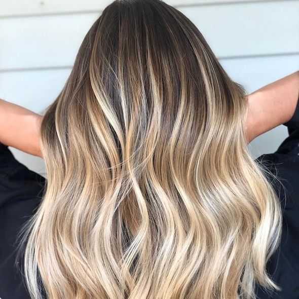 Woman with long, wavy hair; dark roots fade to blonde highlights and ends.