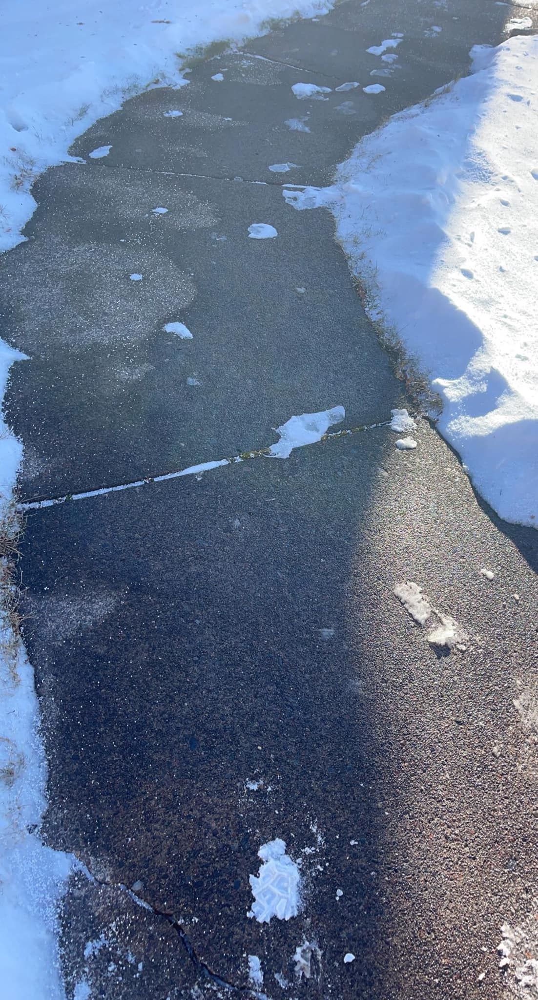 Icy sidewalk with snow along the edge and wet, dark pavement in the center