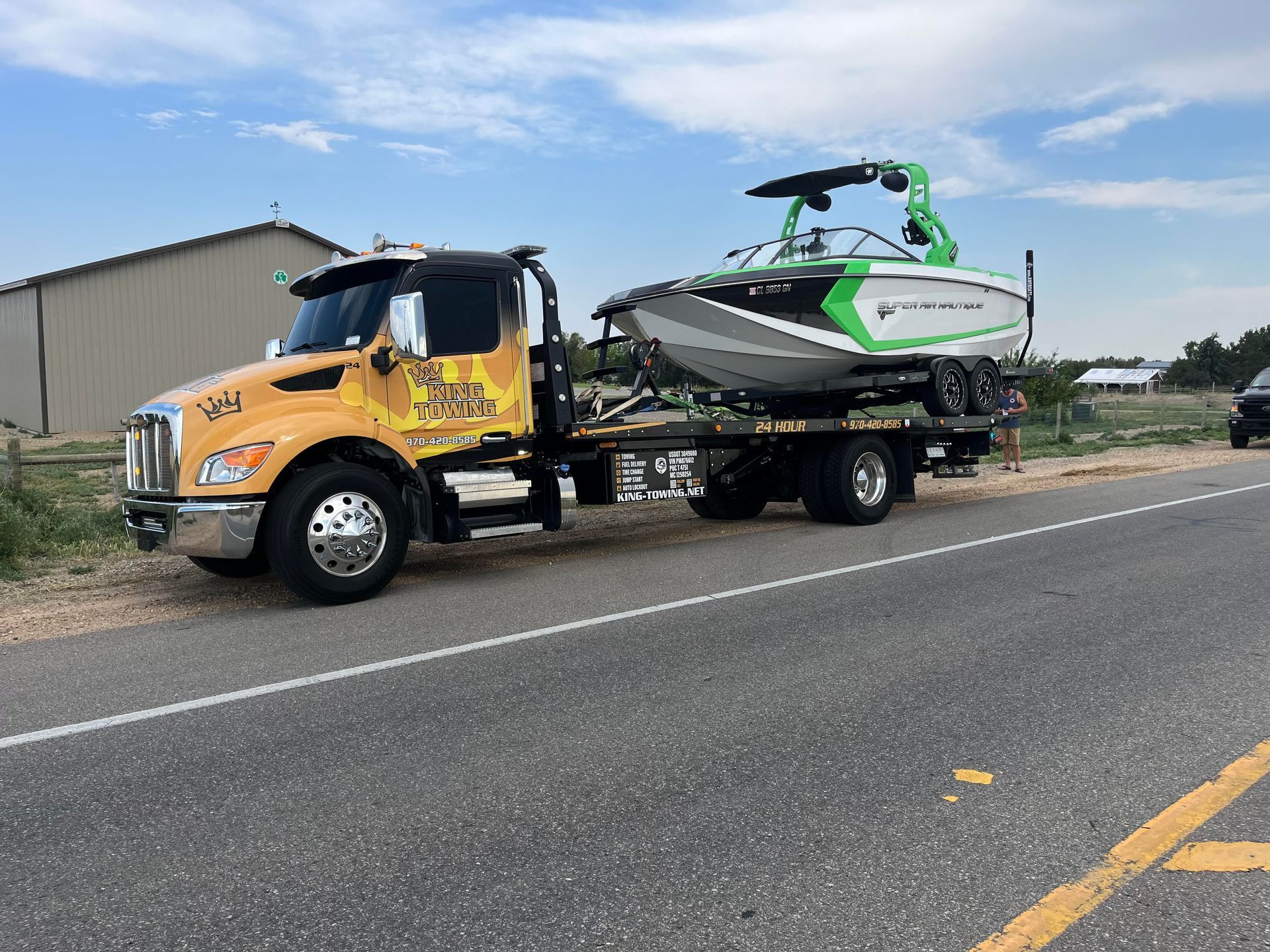 Yellow tow truck hauling a green-and-white jet ski trailer on a rural roadside