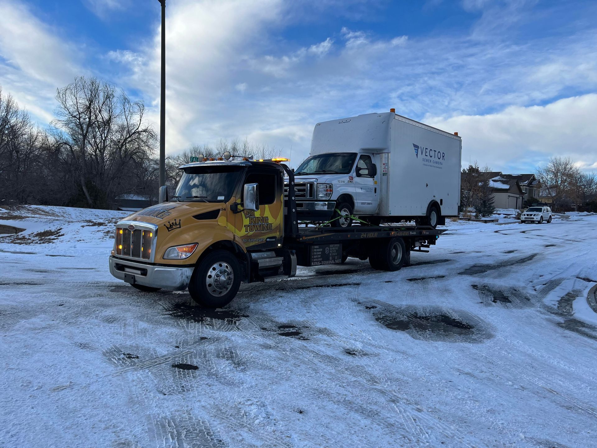 Tow truck carrying a white box truck on a snowy road under a cloudy sky