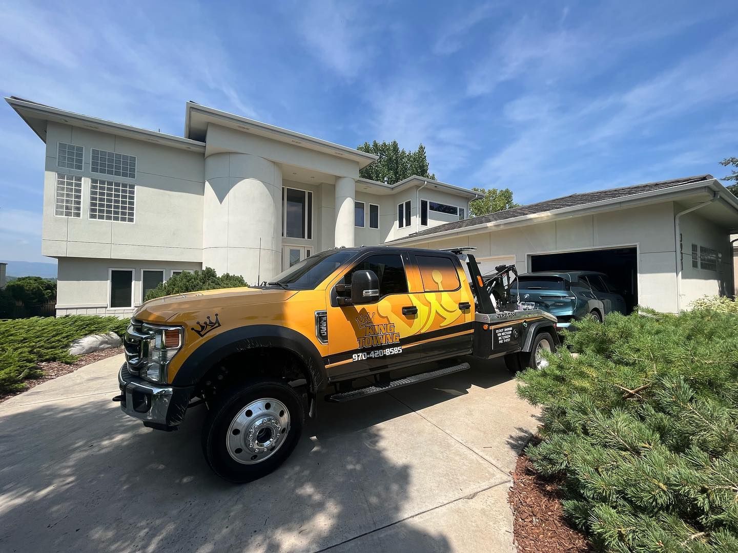 Yellow-and-black pickup truck parked in a driveway beside a white suburban house under a blue sky
