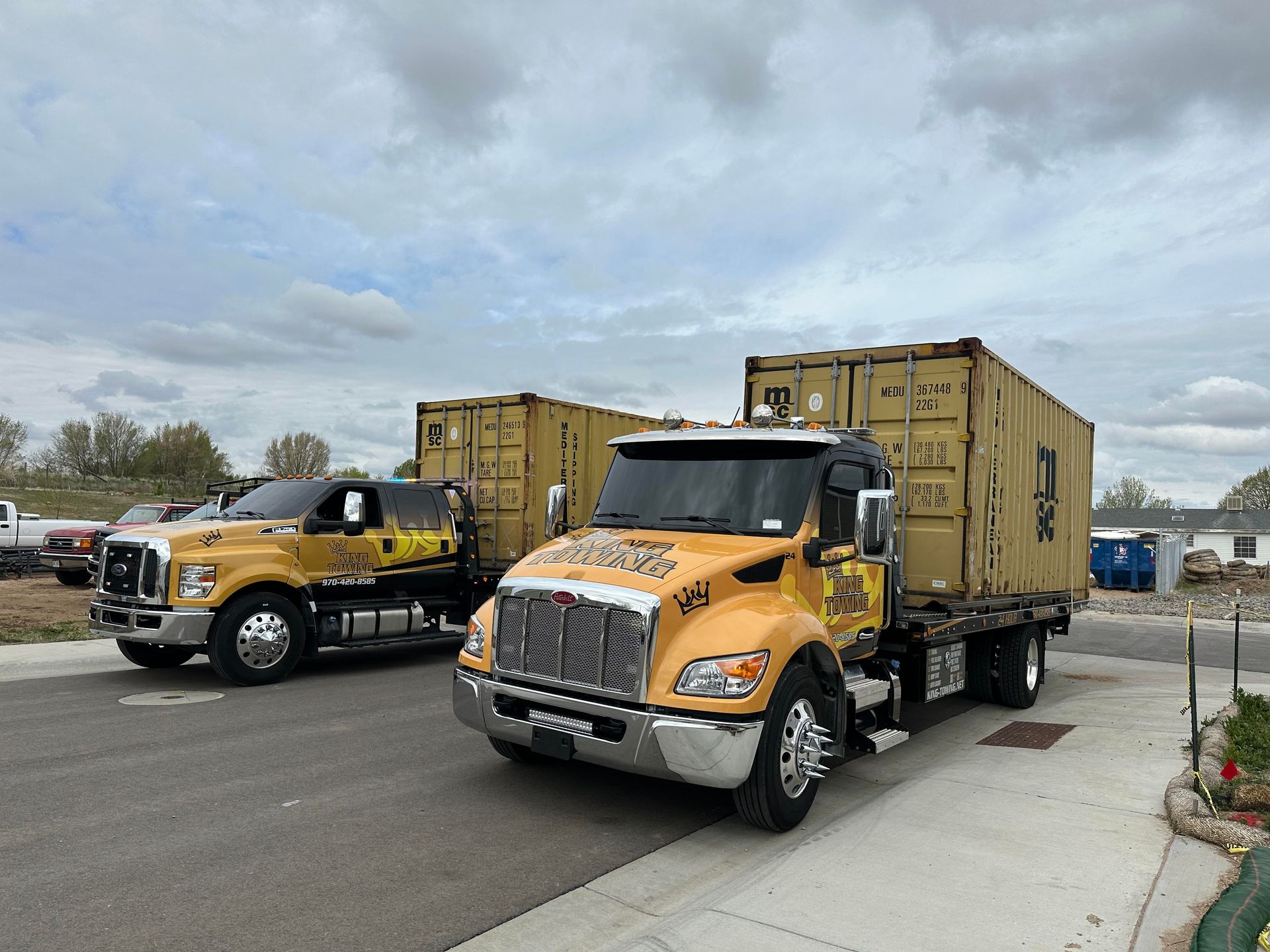 Two yellow box trucks parked on a road under a cloudy sky