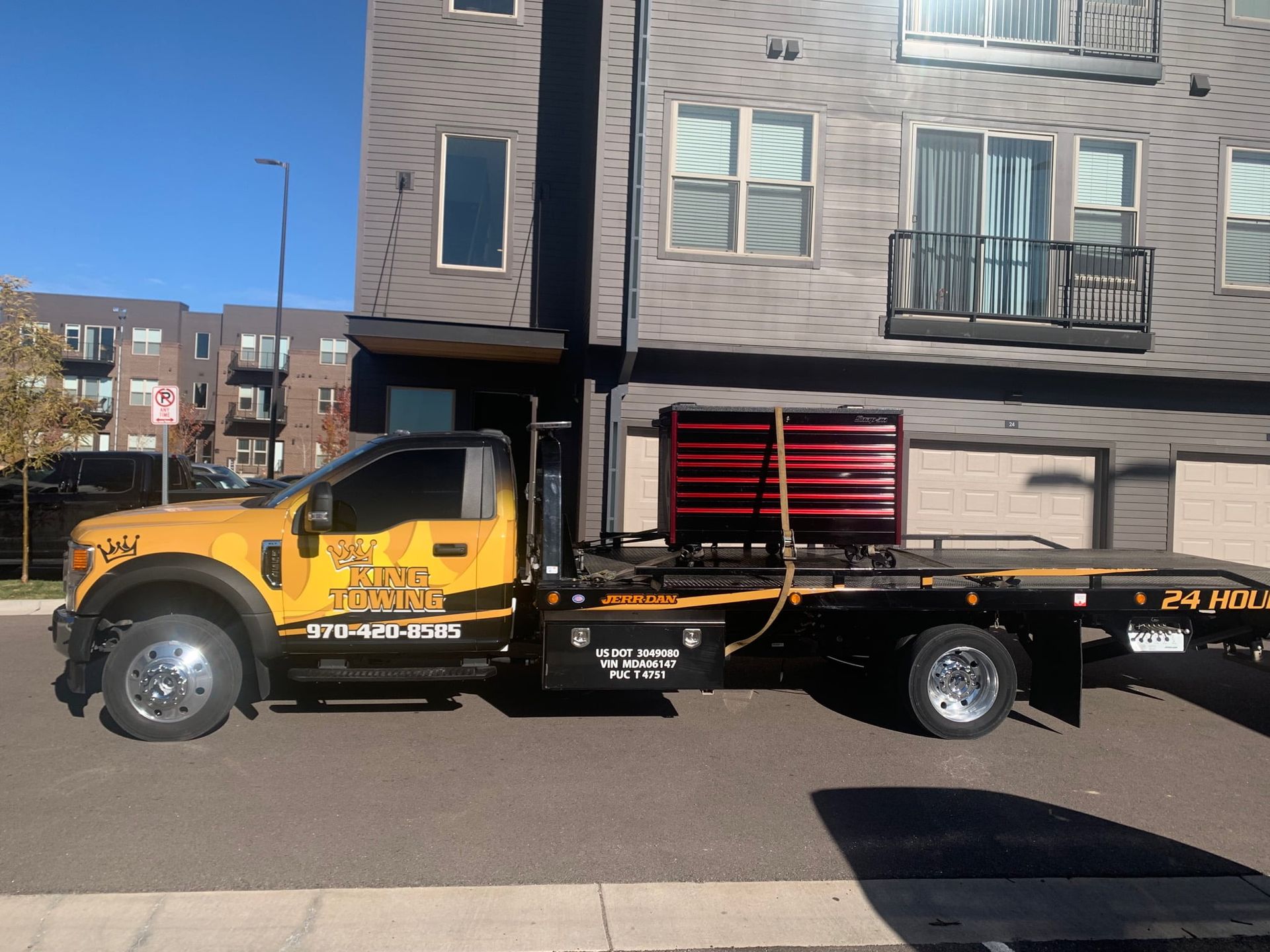 Yellow flatbed tow truck parked on a street beside apartment buildings.
