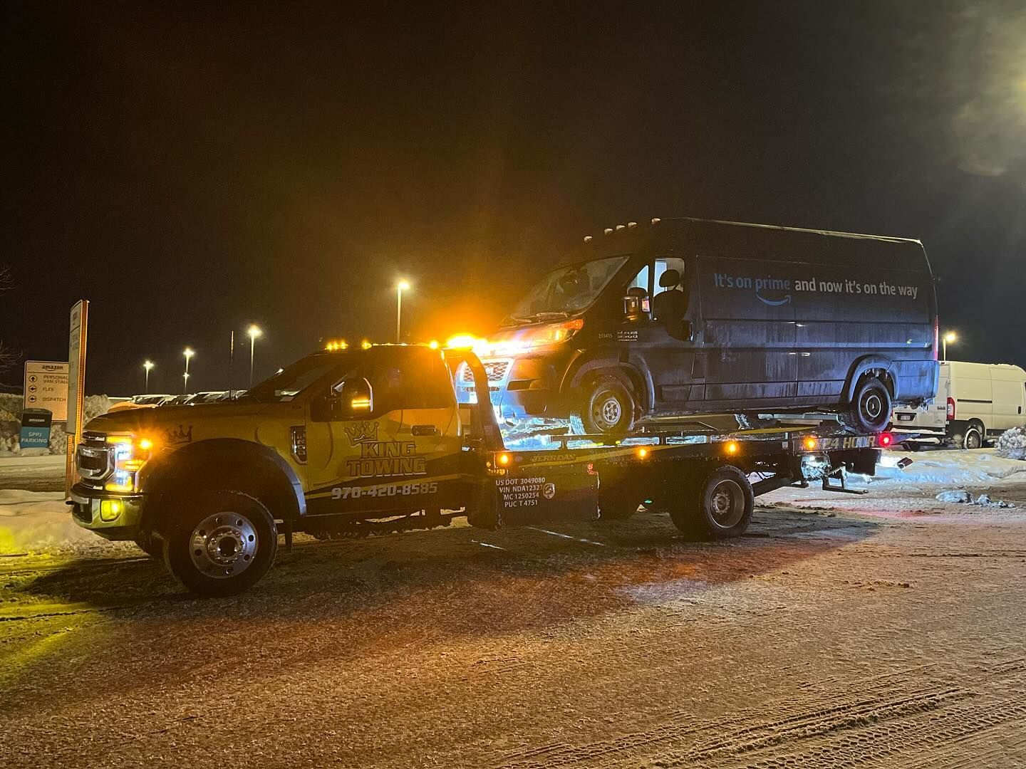 Tow truck loading a dark van at night beside police lights on a wet road