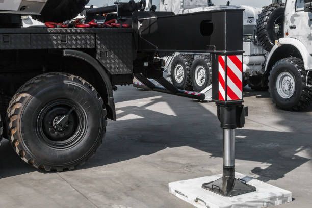 Heavy-duty truck with a stabilizing outrigger extended onto a concrete pad, red-and-white striped safety panel visible.