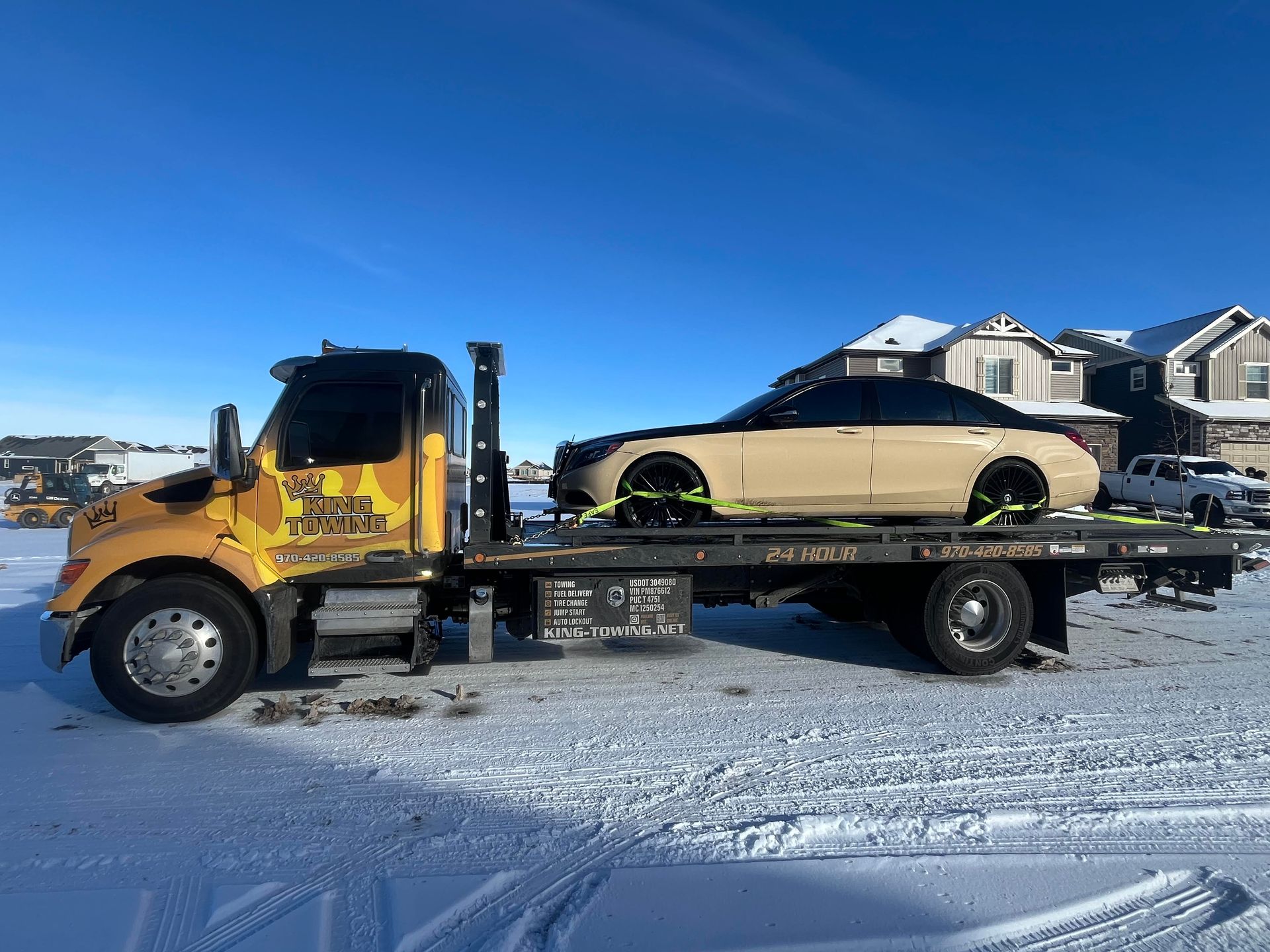 Yellow tow truck hauling a beige SUV on a flatbed in a snowy residential area