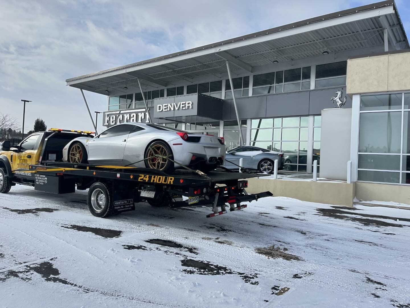 Tow truck carrying a silver car outside a DENVER dealership on a snowy lot