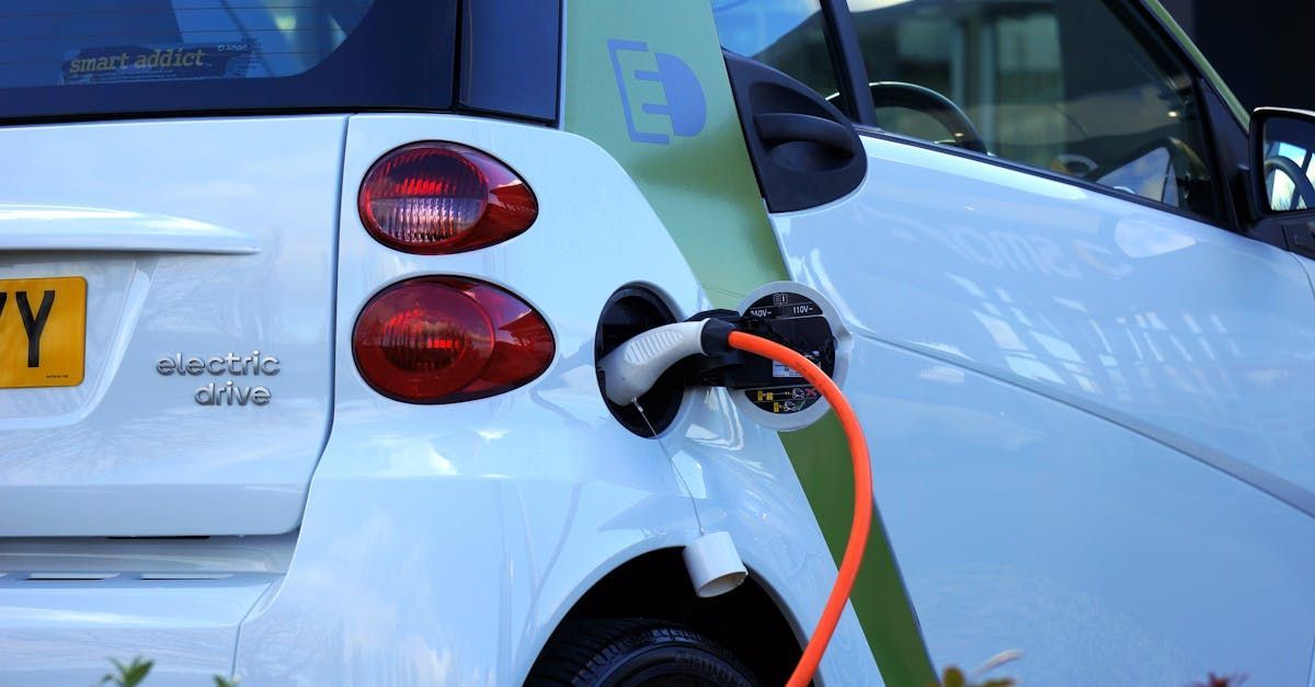 White electric car plugged into a charging station with an orange cable outdoors