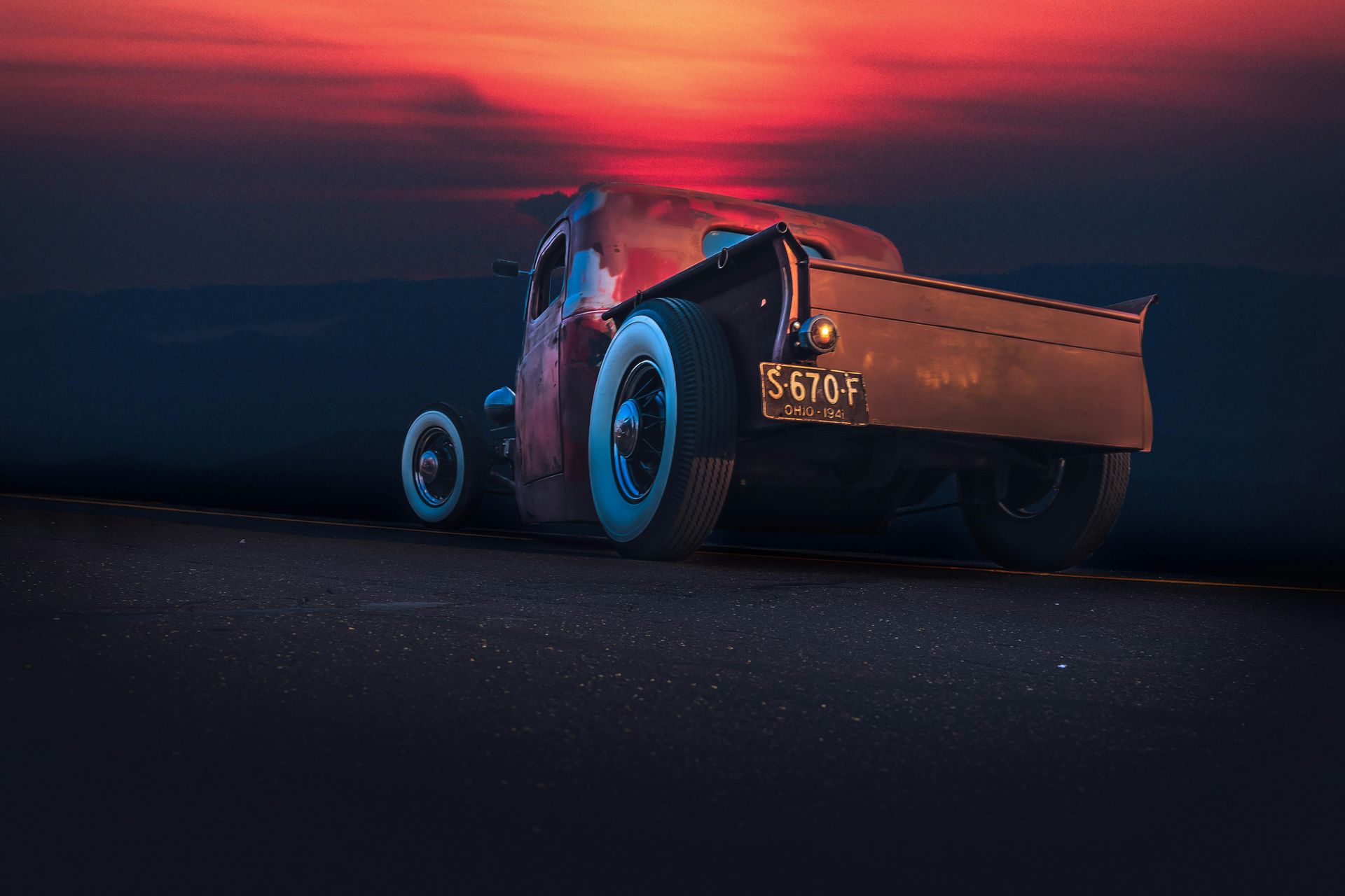 Vintage car on a dark road at sunset, glowing red and blue against a dramatic sky