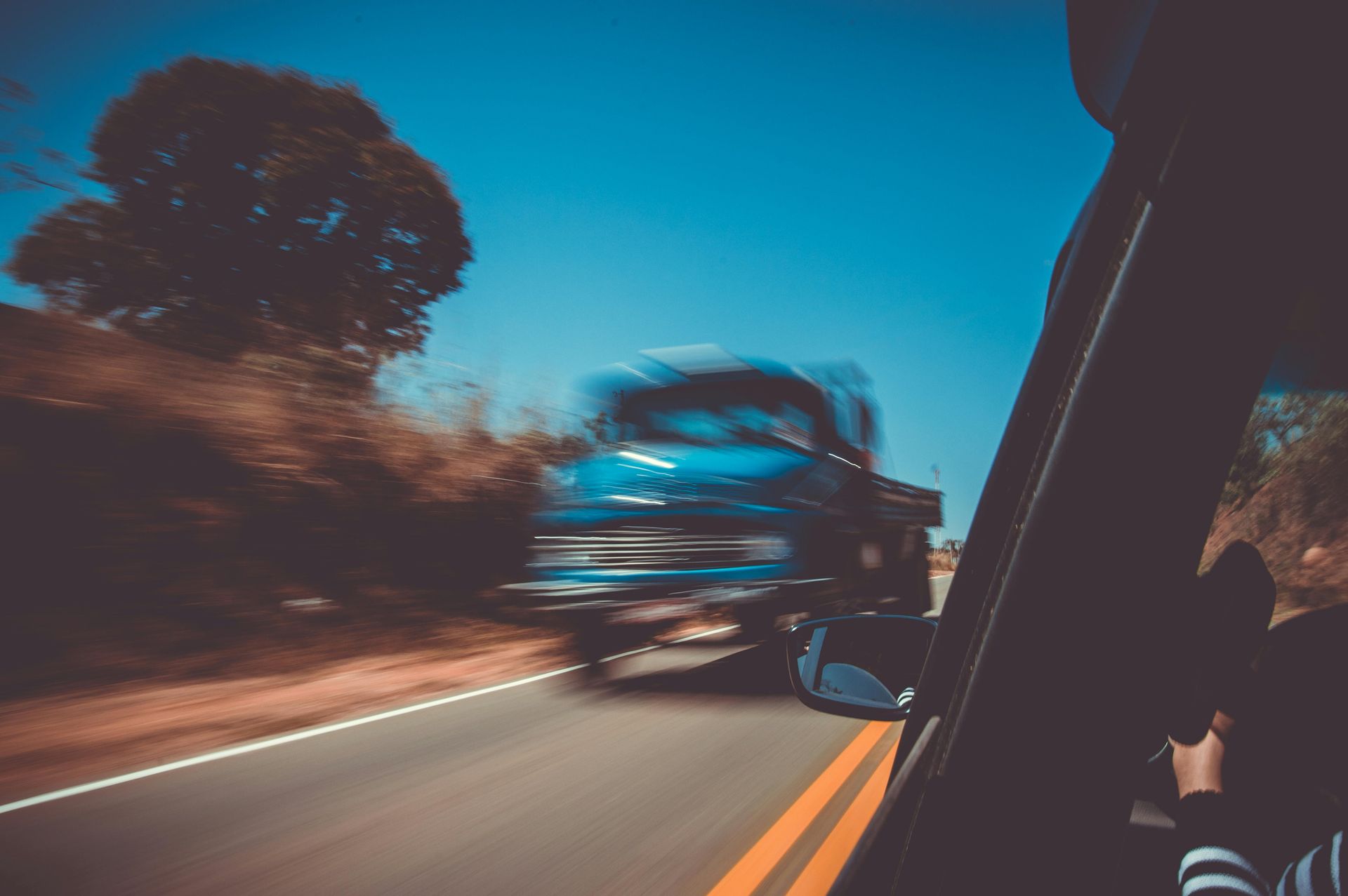 Blurred truck speeding past a car on a curving road at dusk, viewed from inside the vehicle