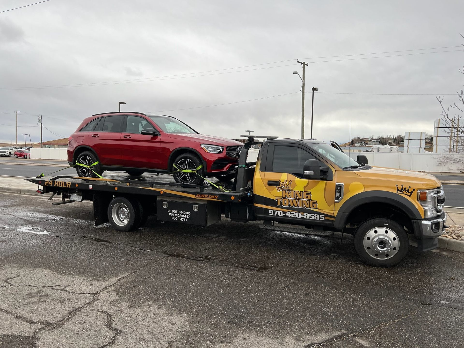 Yellow tow truck carrying a red SUV in a snowy parking lot