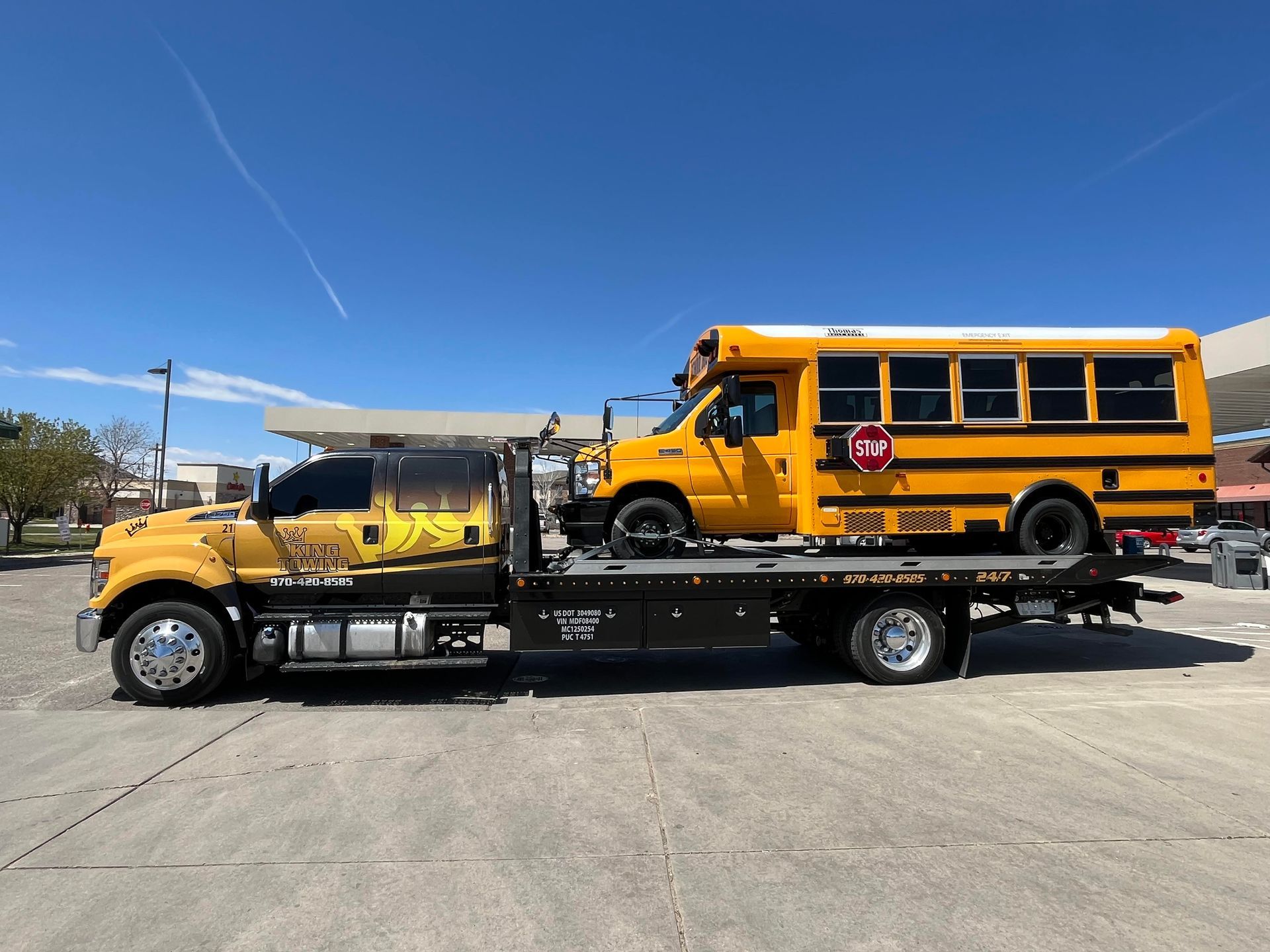 Yellow tow truck carrying a yellow school bus on a flatbed trailer under a blue sky