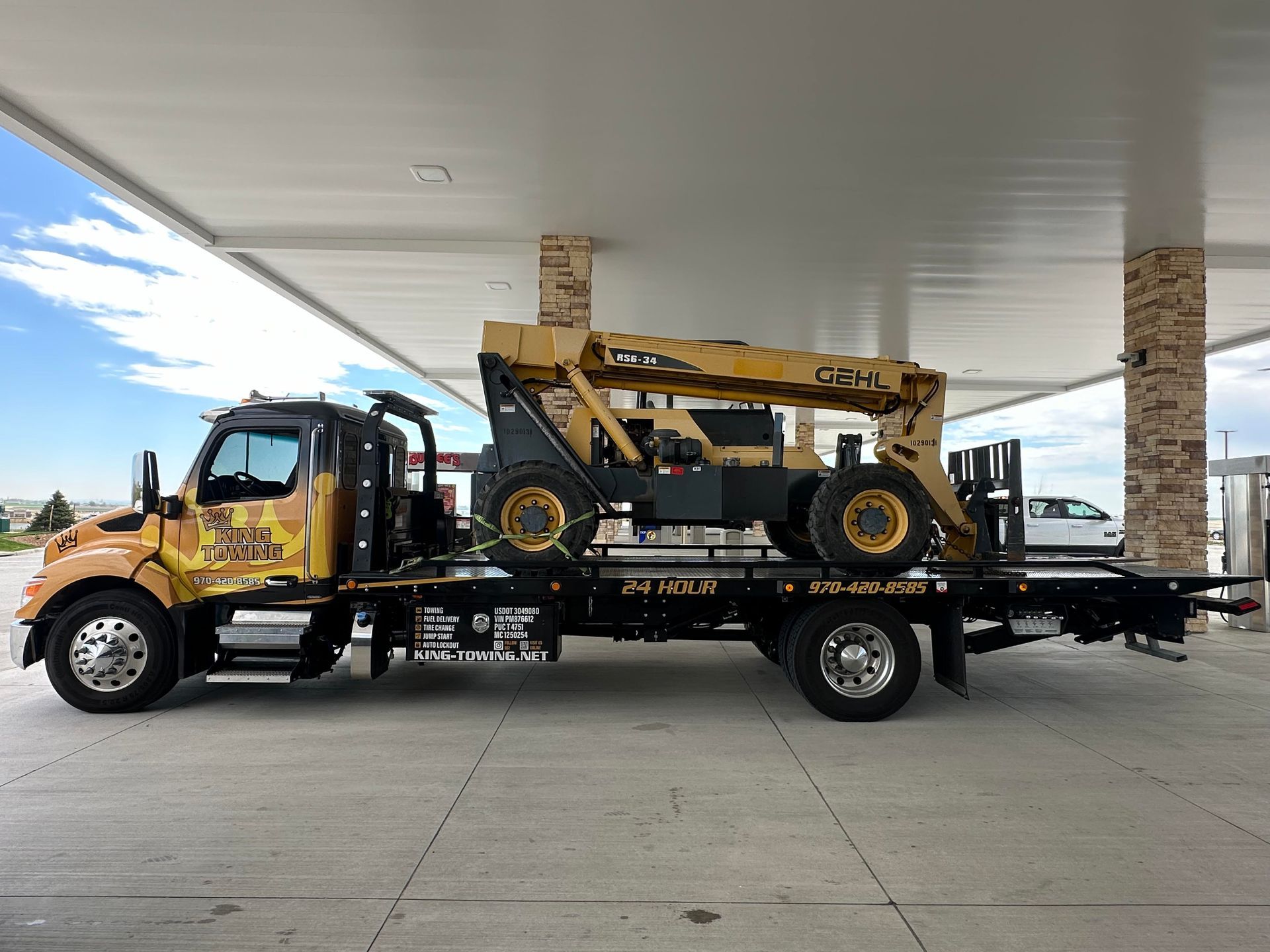 Yellow tow truck carrying a vintage yellow loader under a gas station canopy