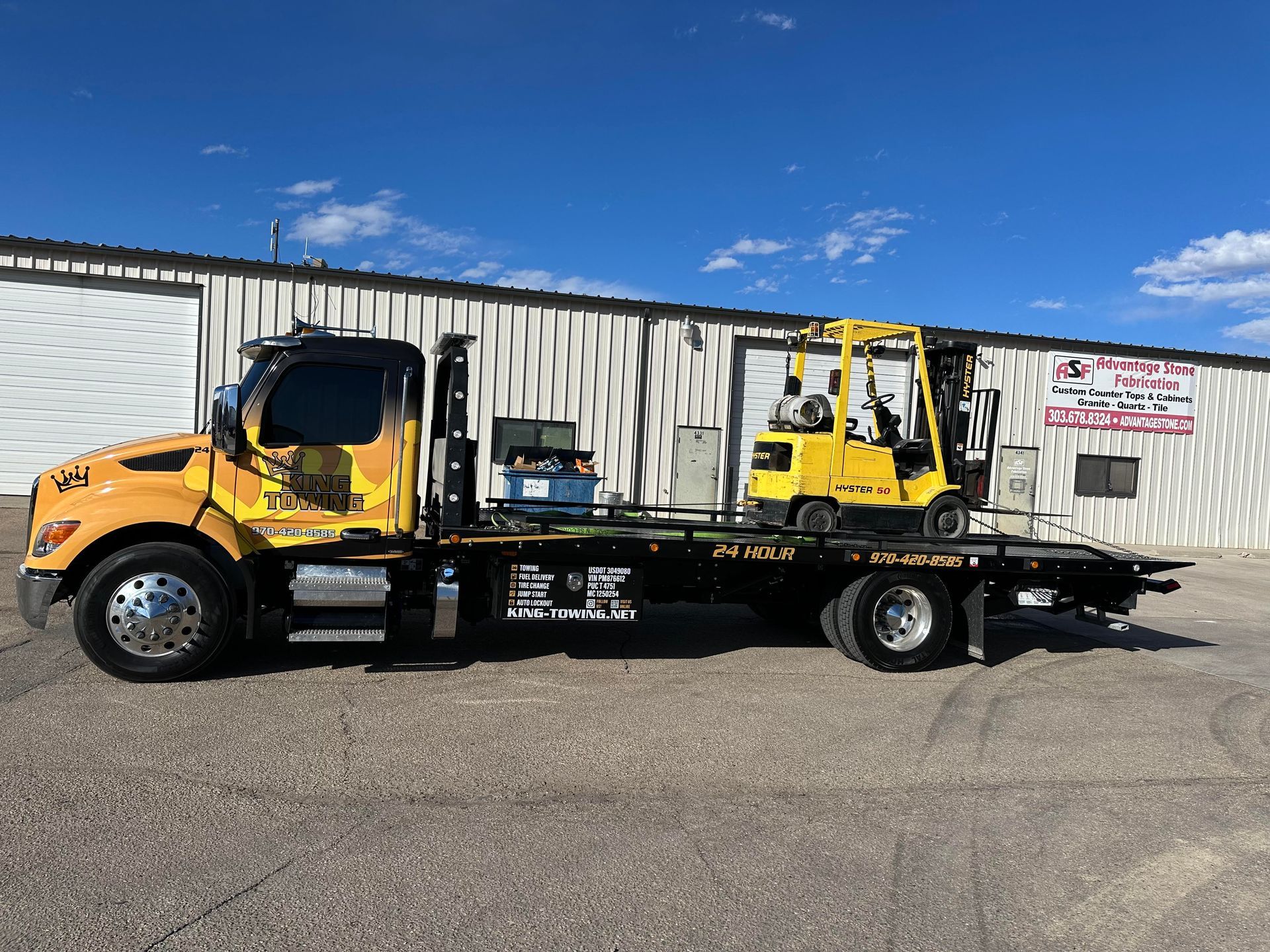 Yellow tow truck carrying a black car on a flatbed in an industrial lot