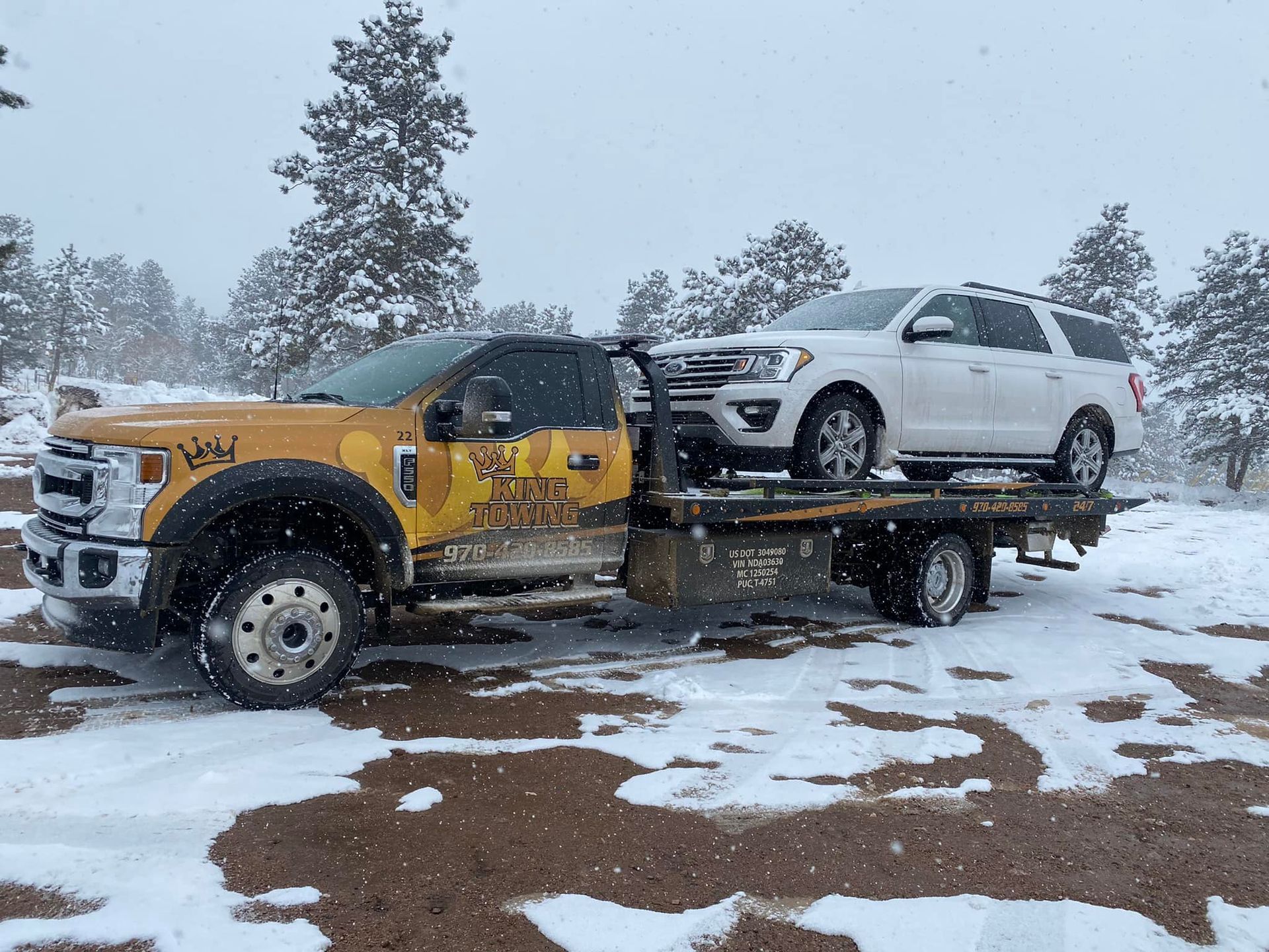 Tow truck hauling a white SUV on a snowy roadside with pine trees in the background