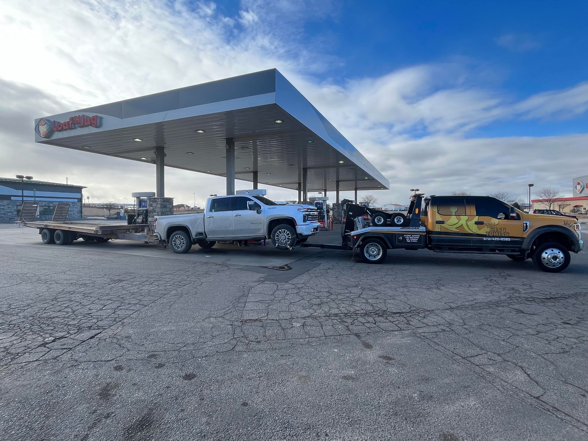 Tow trucks and pickup trucks lined up at a gas station under a blue sky.