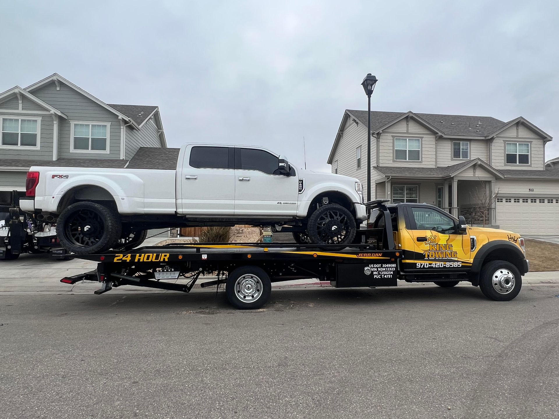 Tow truck carrying a white pickup and a yellow truck on a residential street