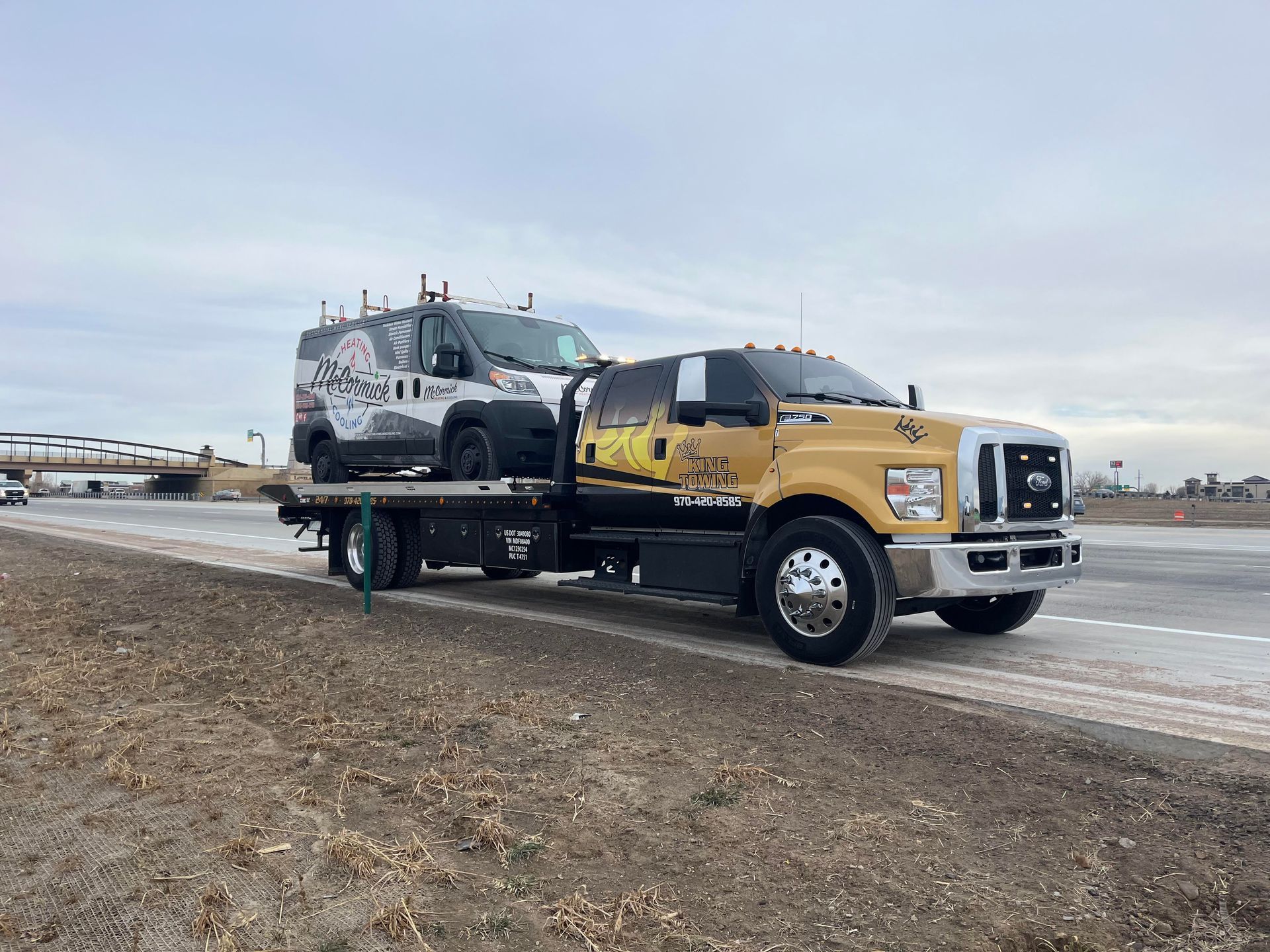 Yellow tow truck hauling a black SUV on a flatbed beside a snowy roadside