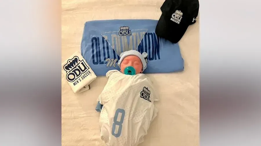 A baby is laying on a bed next to a hat and a t-shirt.