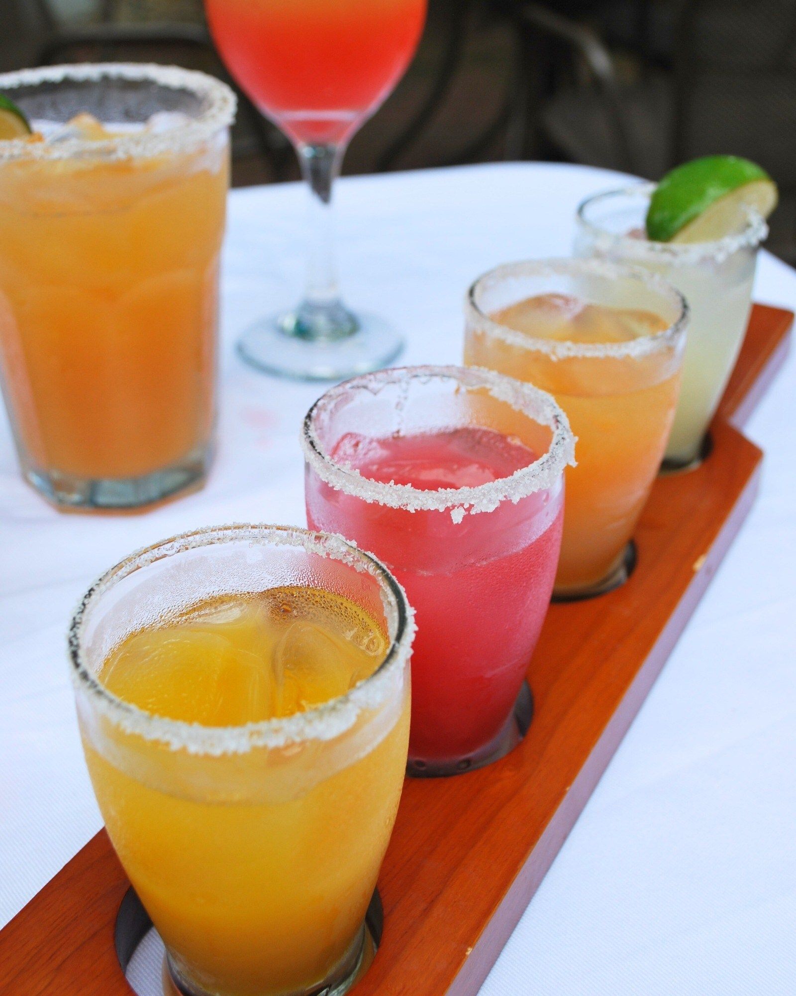 A row of shot glasses with different colored liquids on a wooden tray
