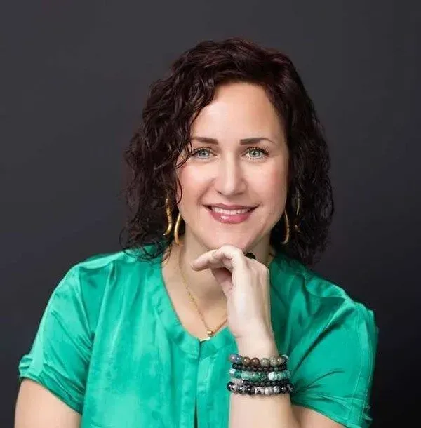 A woman in a green shirt is smiling with her hand on her chin.