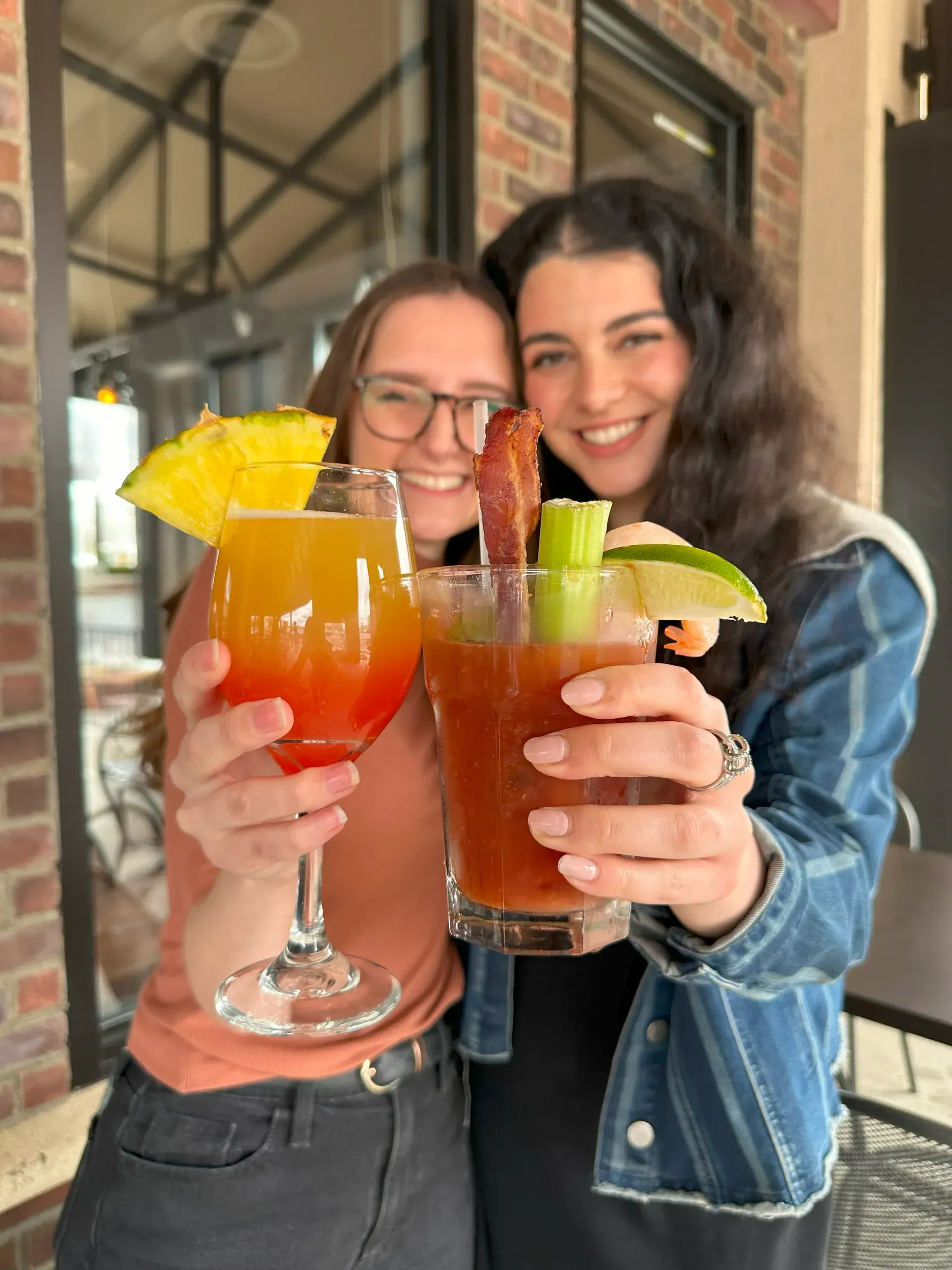 Two people clink colorful tropical drinks and smile in a cozy café.