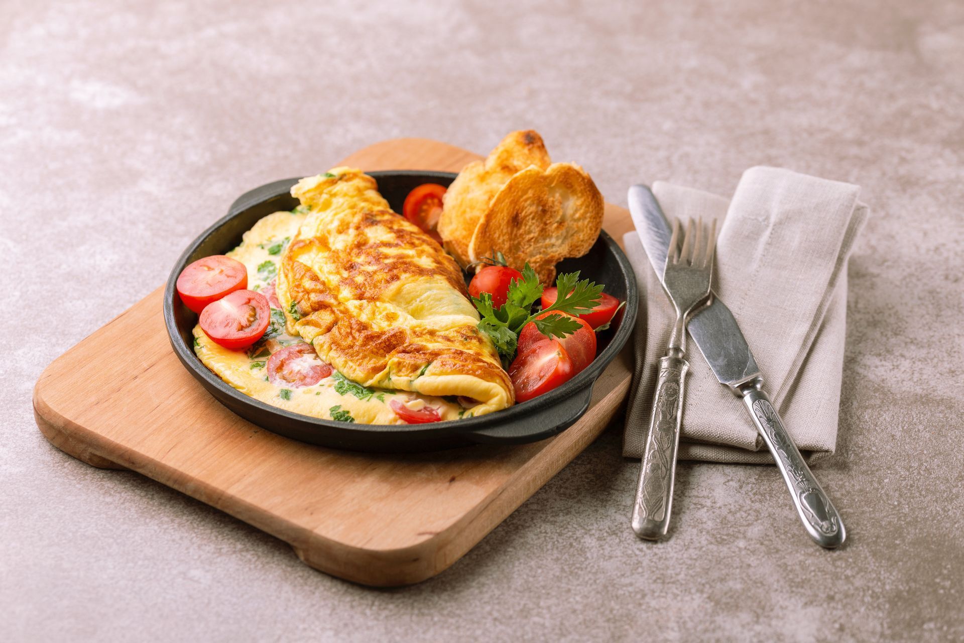 An omelet with tomatoes and bread on a pan on a wooden cutting board.