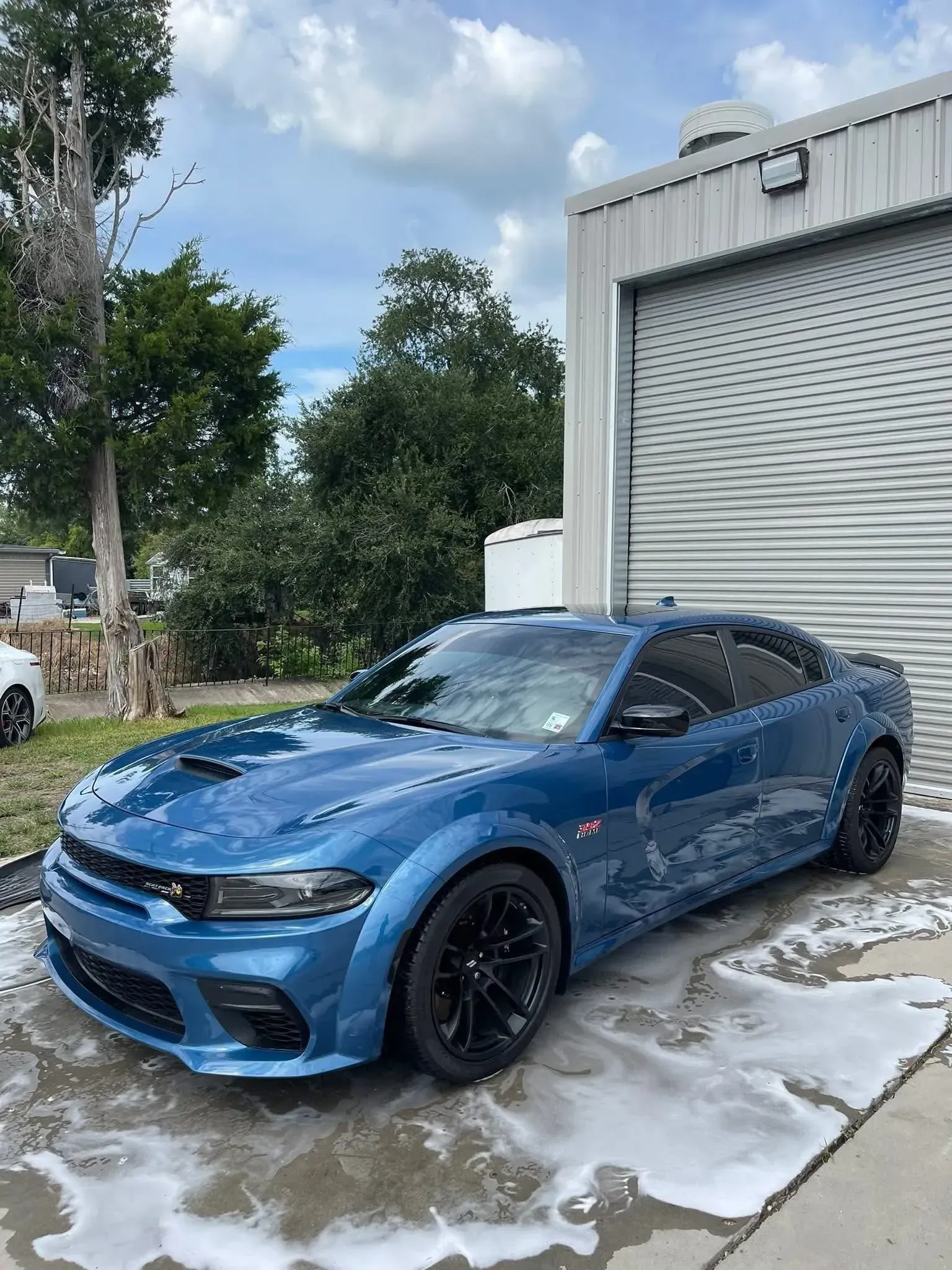 Blue Dodge Charger parked outside a building, covered in soapy suds. Black wheels, sunny day.