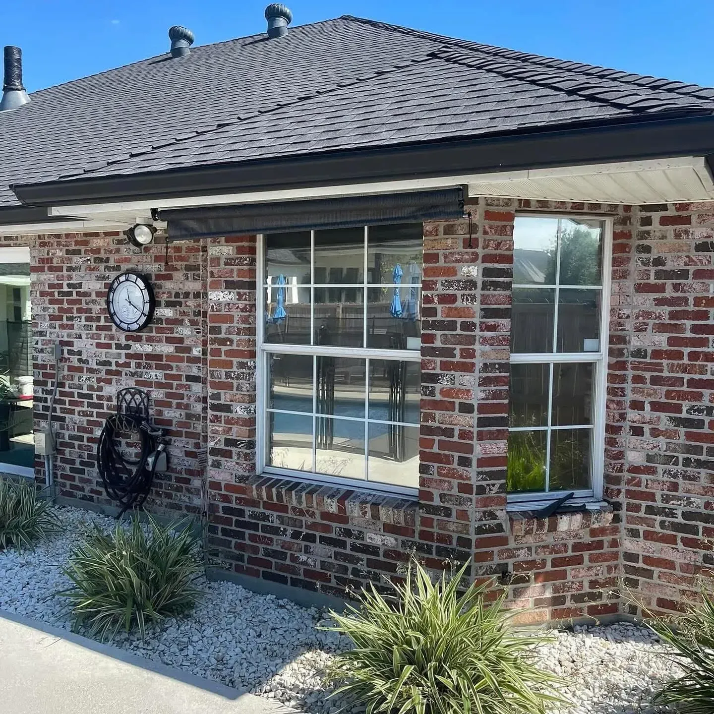 Brick building exterior with two windows, a clock, and shrubbery.
