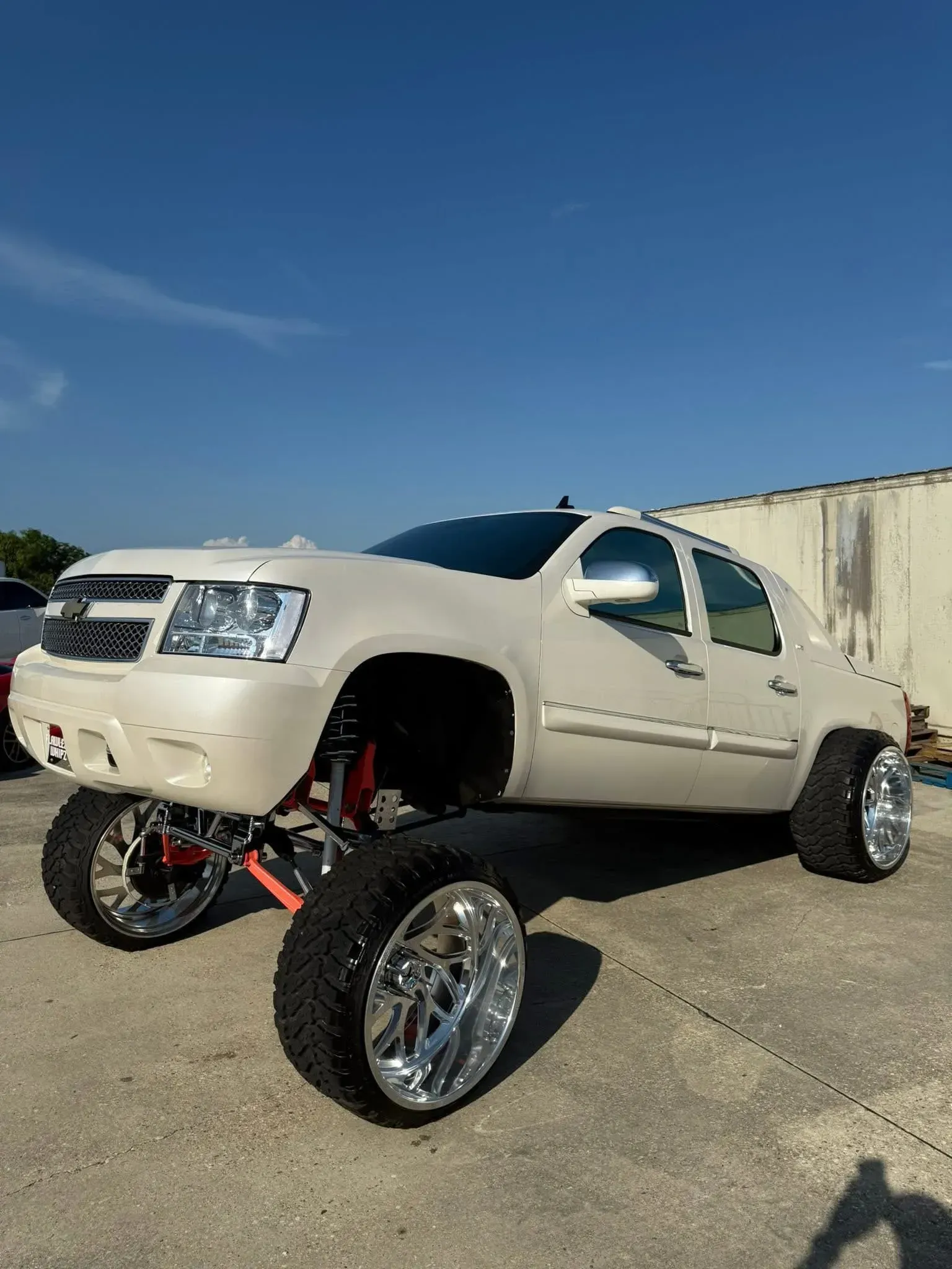 White lifted Chevy Avalanche truck with chrome wheels against a blue sky.