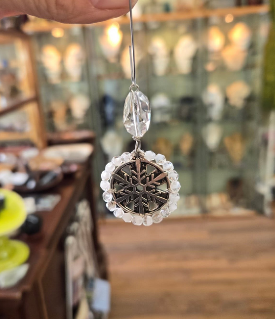 Silver snowflake ornament with clear crystal beads, held in front of a shop interior.