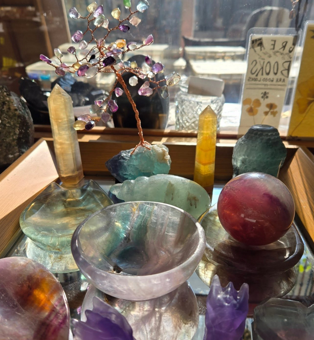 Display of colorful crystals: spheres, towers, and a bowl, with a copper wire tree, on a reflective surface.