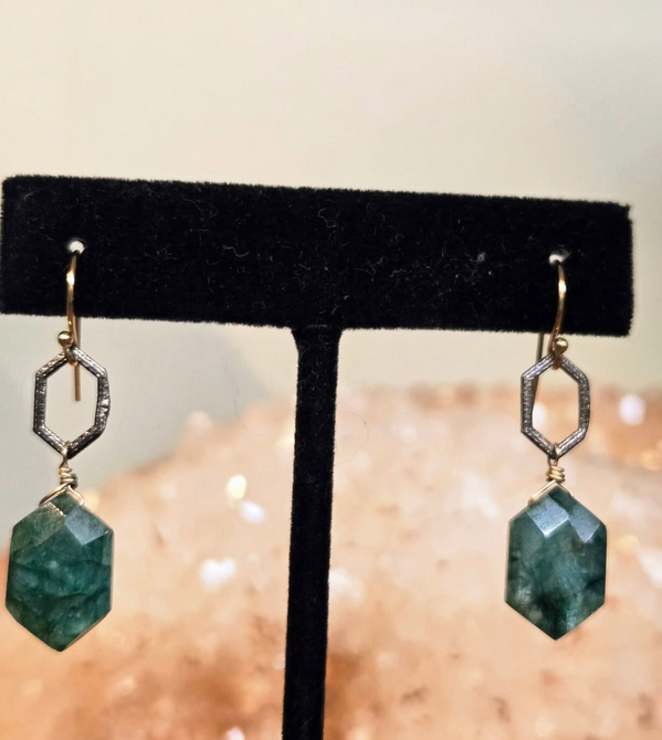 Pair of green faceted gemstone earrings with hexagonal silver and gold accents on a black display stand.