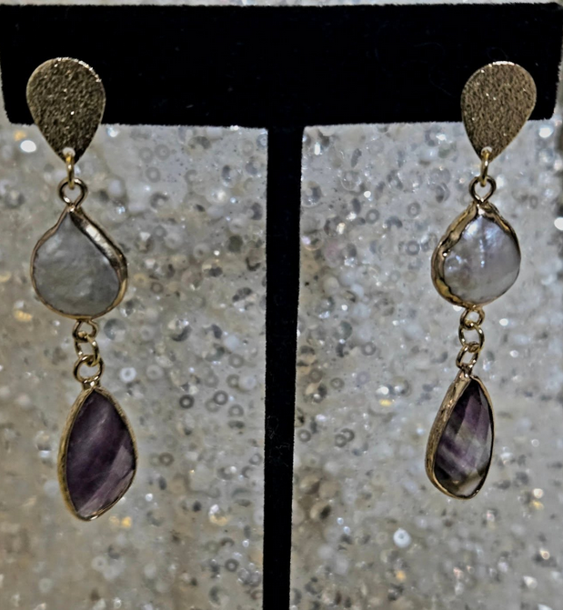 Gold earrings with textured top, white stone, and purple stone drops, displayed on a black stand.