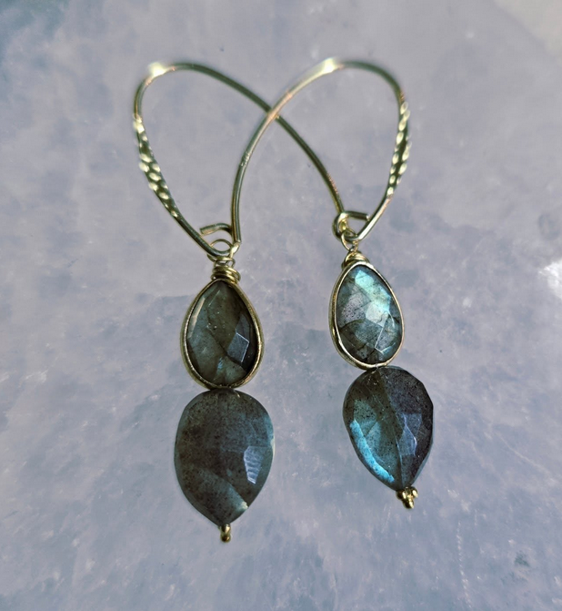Labradorite teardrop earrings on a light blue-white surface. Gold wire twists into ear hooks.