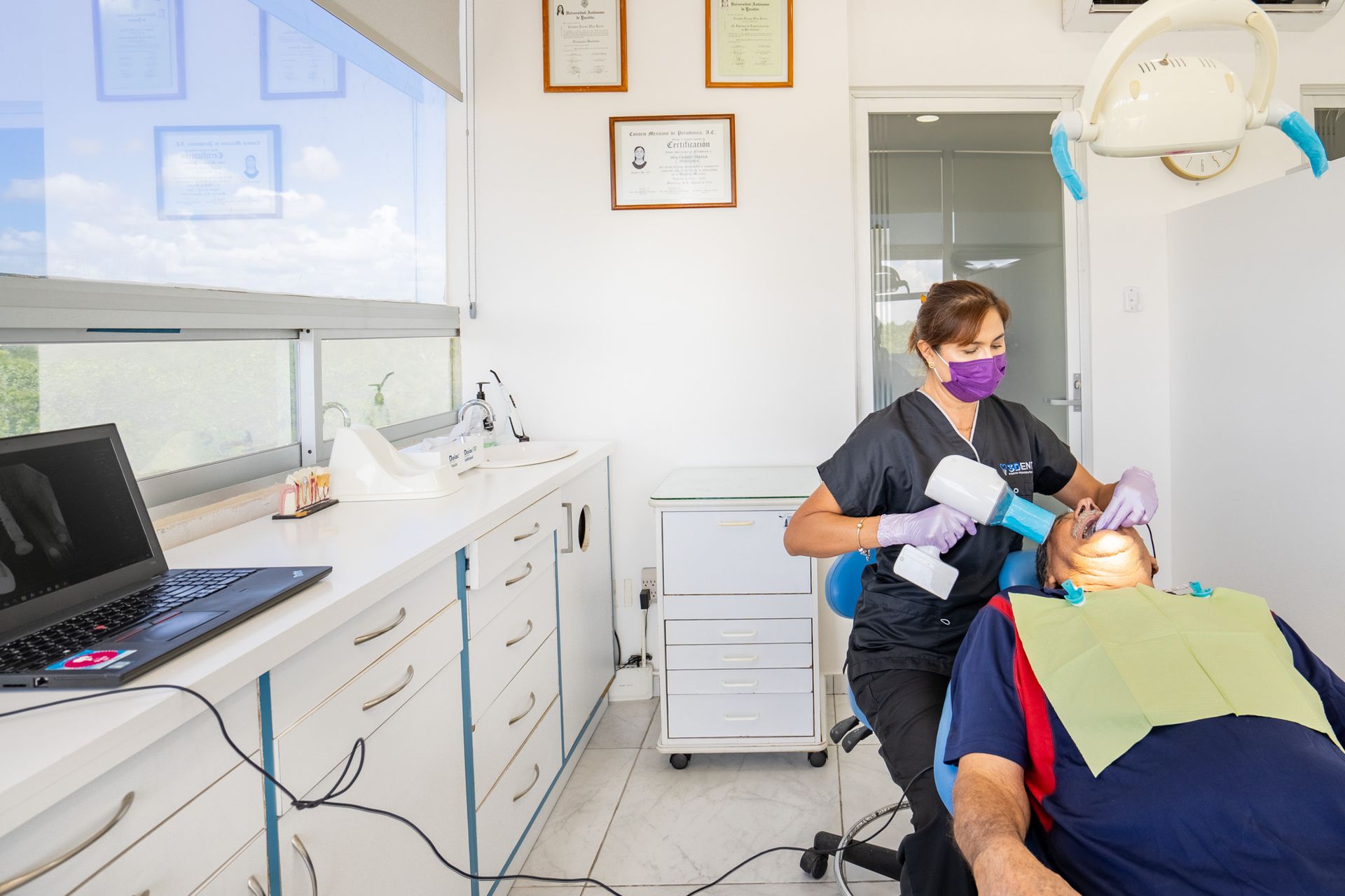 Dentista examinando a un paciente en una clínica dental, con monitor y luz superior visibles.