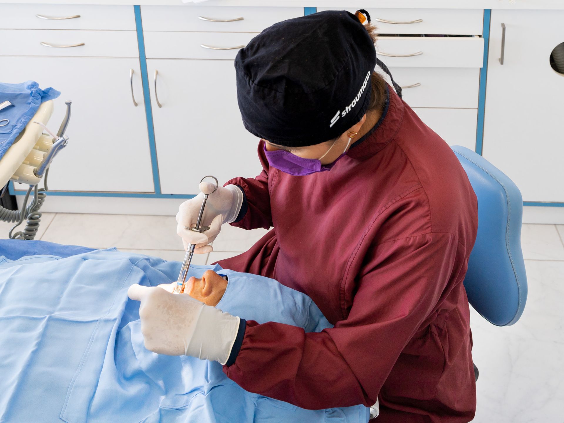 Dentista con uniforme quirúrgico color granate atendiendo a un paciente en el sillón dental.