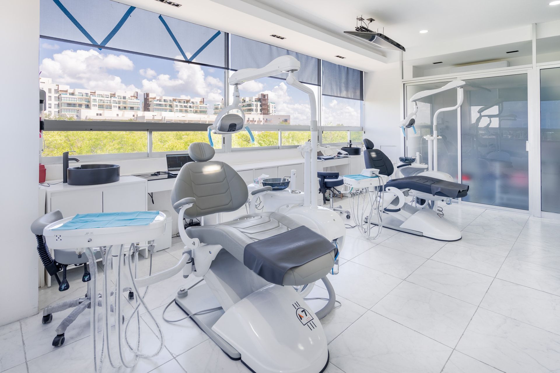 Clínica dental luminosa con sillones, instrumental y grandes ventanales con vistas a la ciudad.