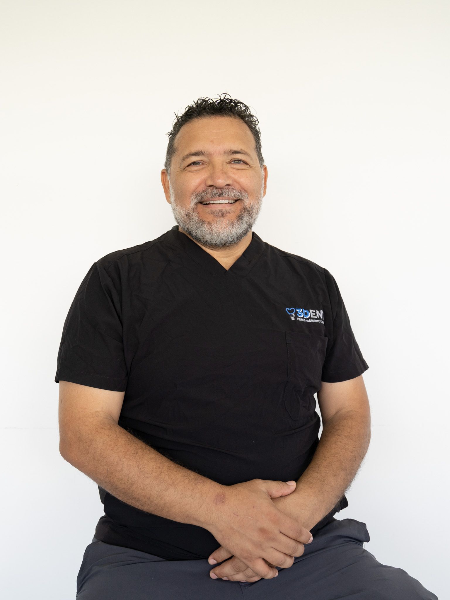 Hombre sonriente con camiseta negra sentado sobre un fondo blanco liso.