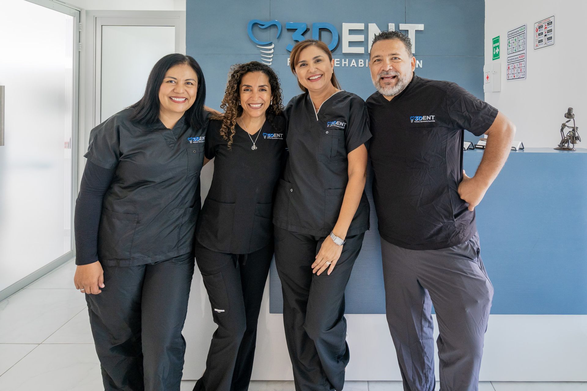 Cuatro miembros del personal con uniformes negros sonríen en la recepción de una clínica.