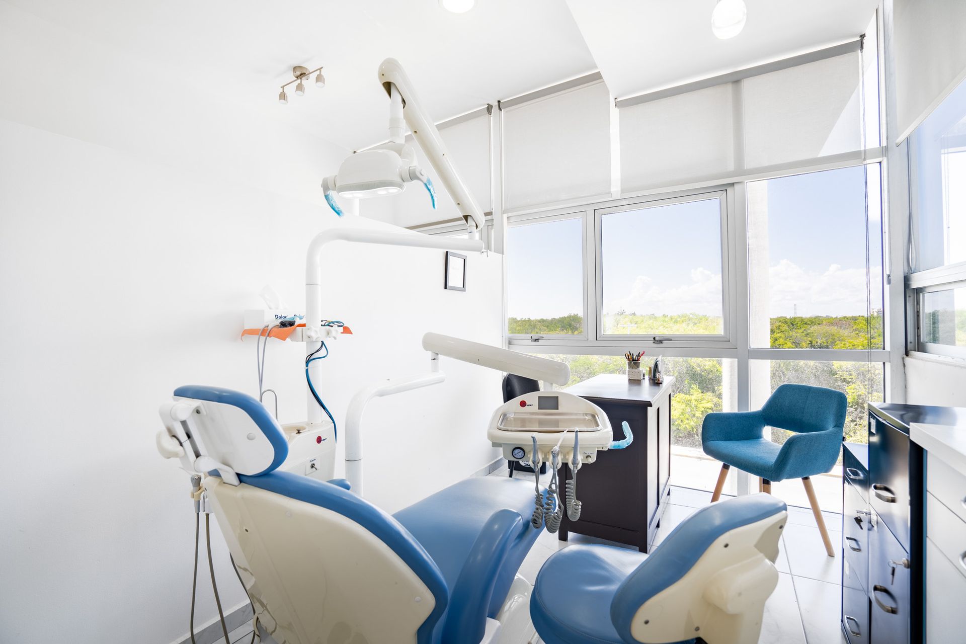 Clínica dental luminosa con sillones blancos, detalles en azul y grandes ventanales con vistas a zonas verdes.