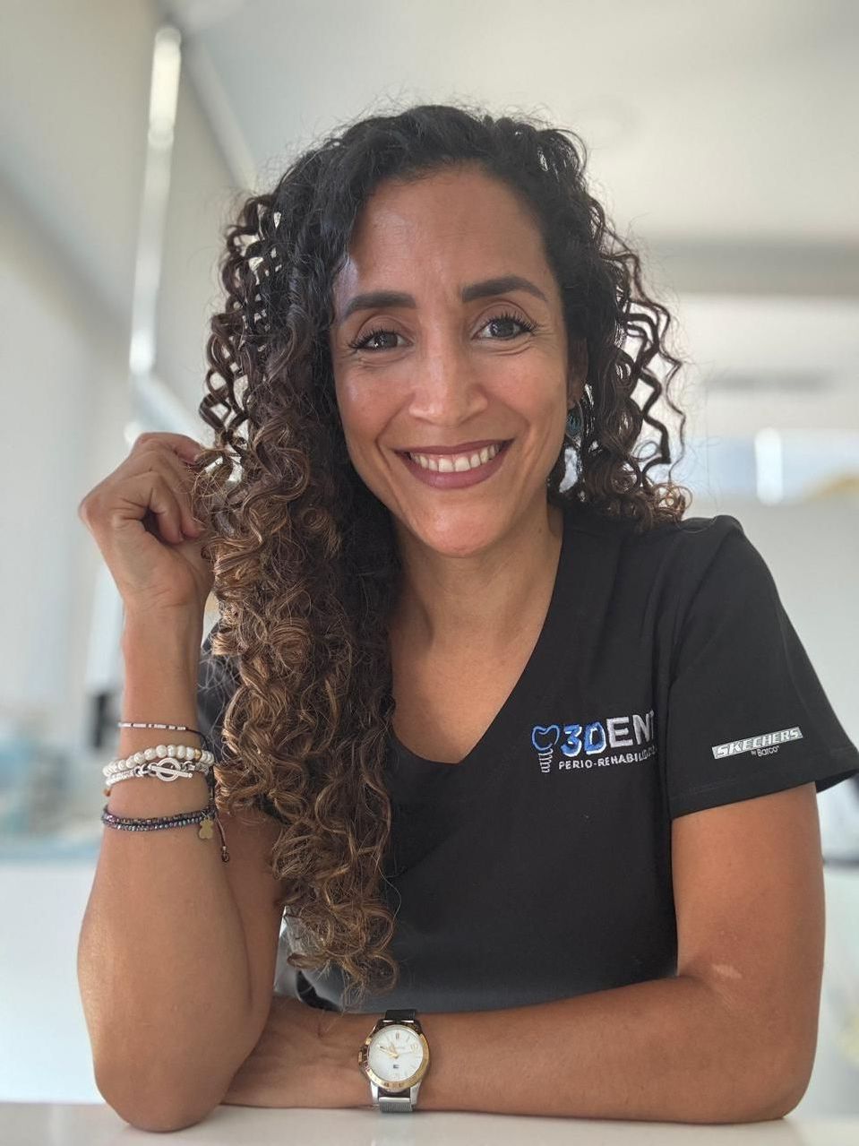 Una persona sonriente con una camiseta negra está apoyada en una mesa en un pasillo luminoso.
